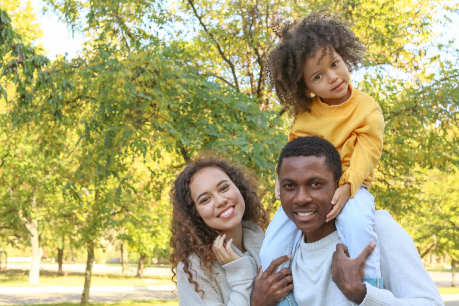 Father carrying his daughter on his shoulders beside her mother in a park