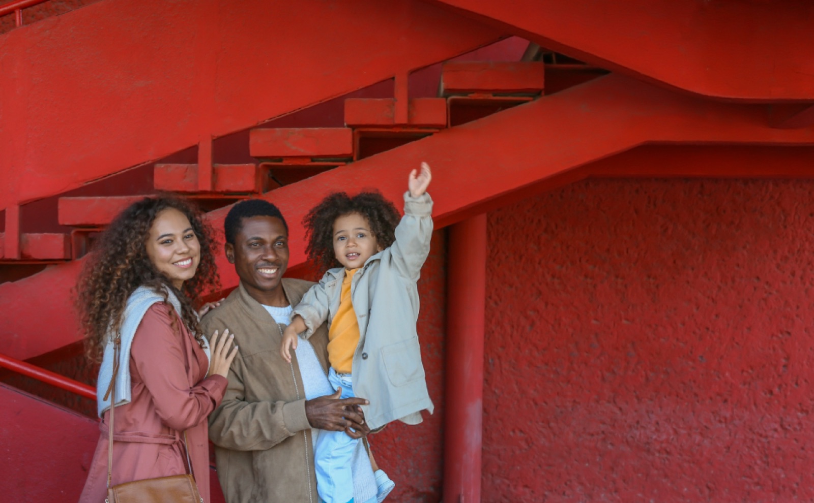 Young family laughing in front of a red staircase