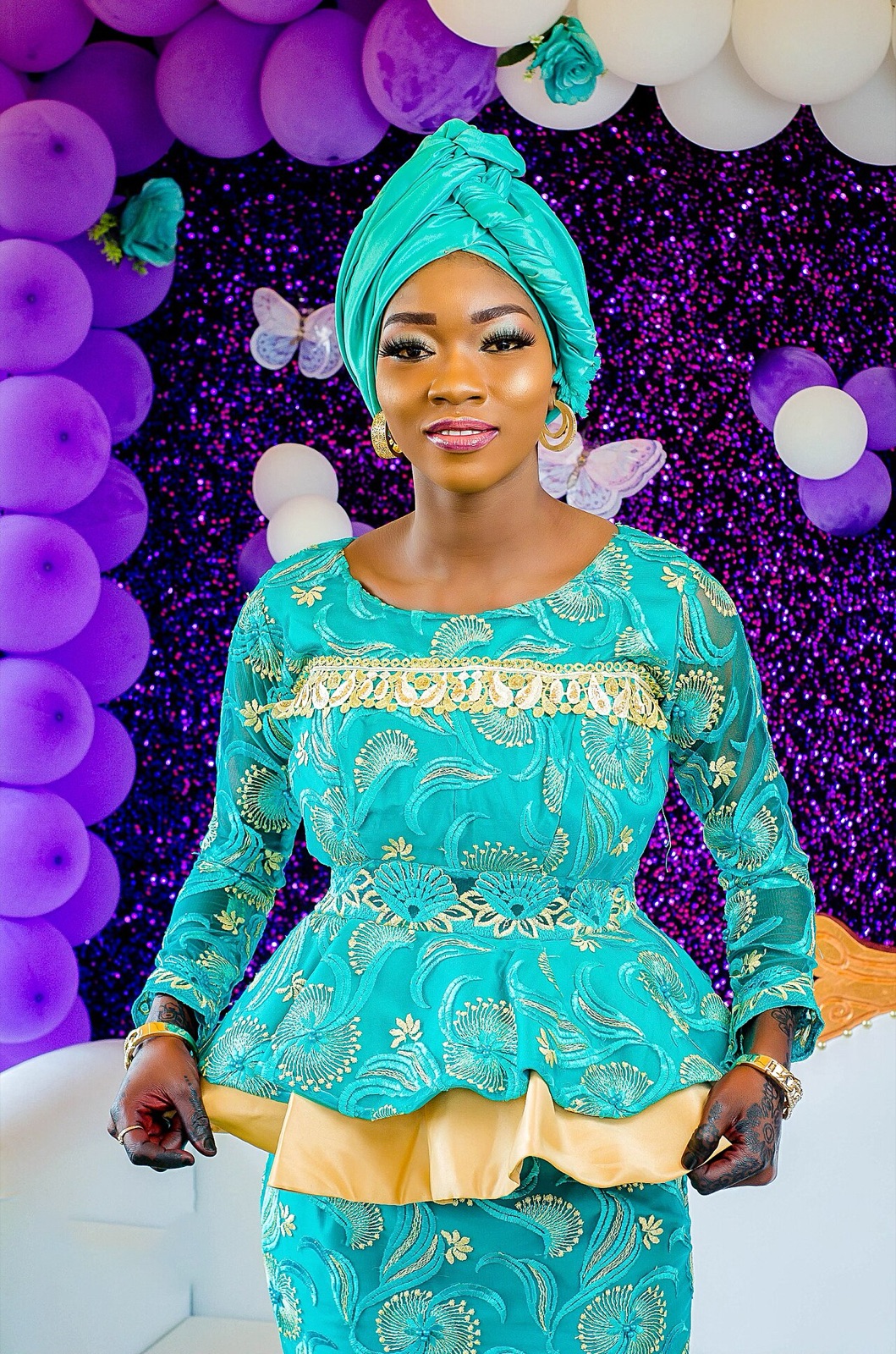 Woman in a teal lace outfit before a purple balloon backdrop
